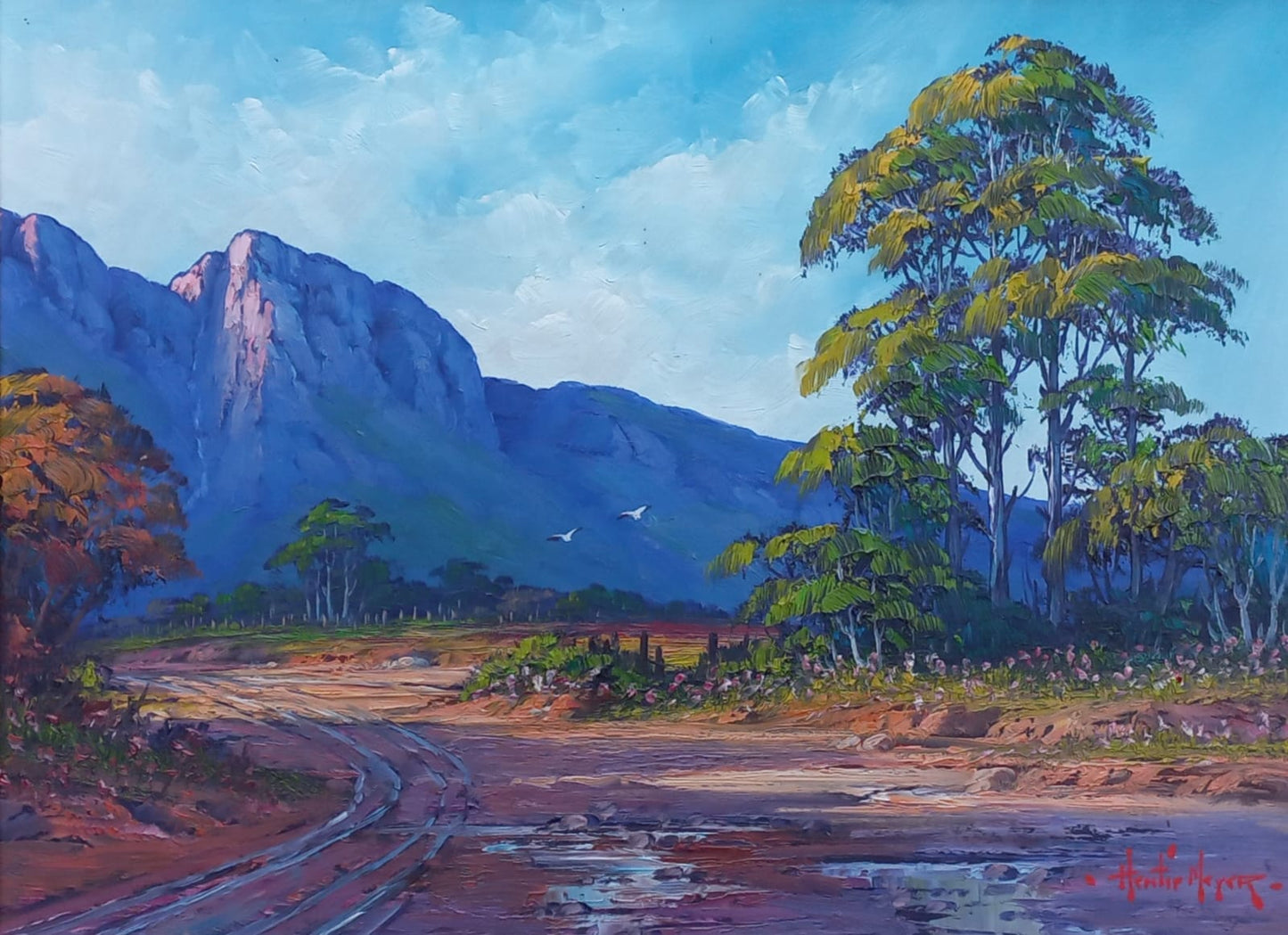 Oil painting of a mountain valley with two birds flying above, a winding dirt road below, and lush green trees against a bright blue sky.